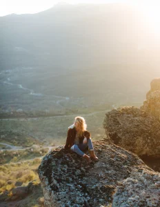 A girl with her hair to one side sitting on the rock in the mountains