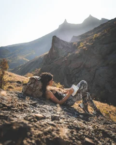 A girl writing her journal while leaning on a rock in the mountain