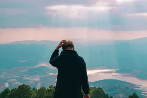 A hiker holding his hair at top of mountain