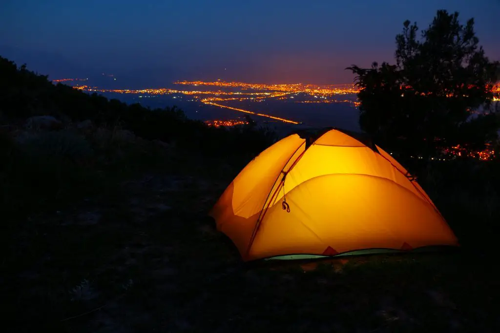 A photo of a tent at night with a city view