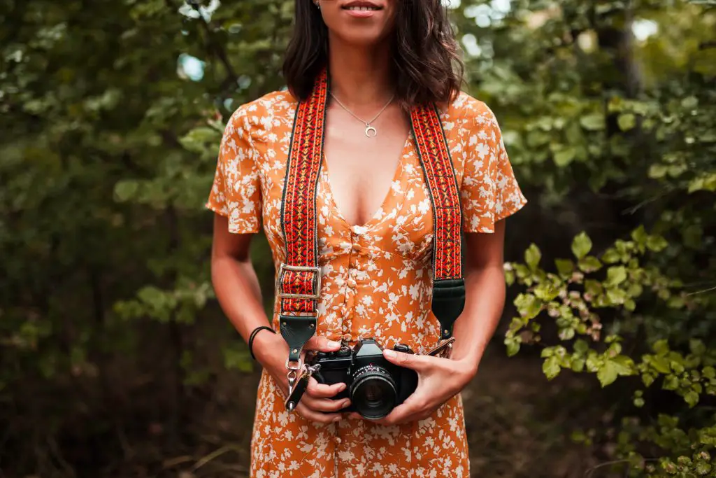A woman holding a camera with an Art Tribute camera strap