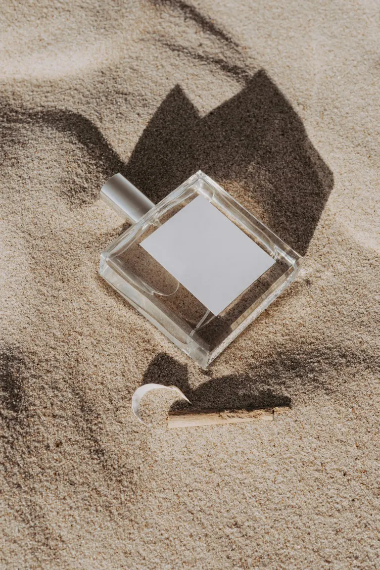 Glass perfume bottle on the sand at another angle