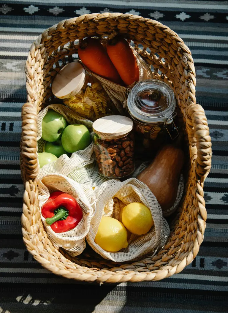Low-key gourmet items photograph of a wicker basket with vegetables and products placed on the table on a sunny day