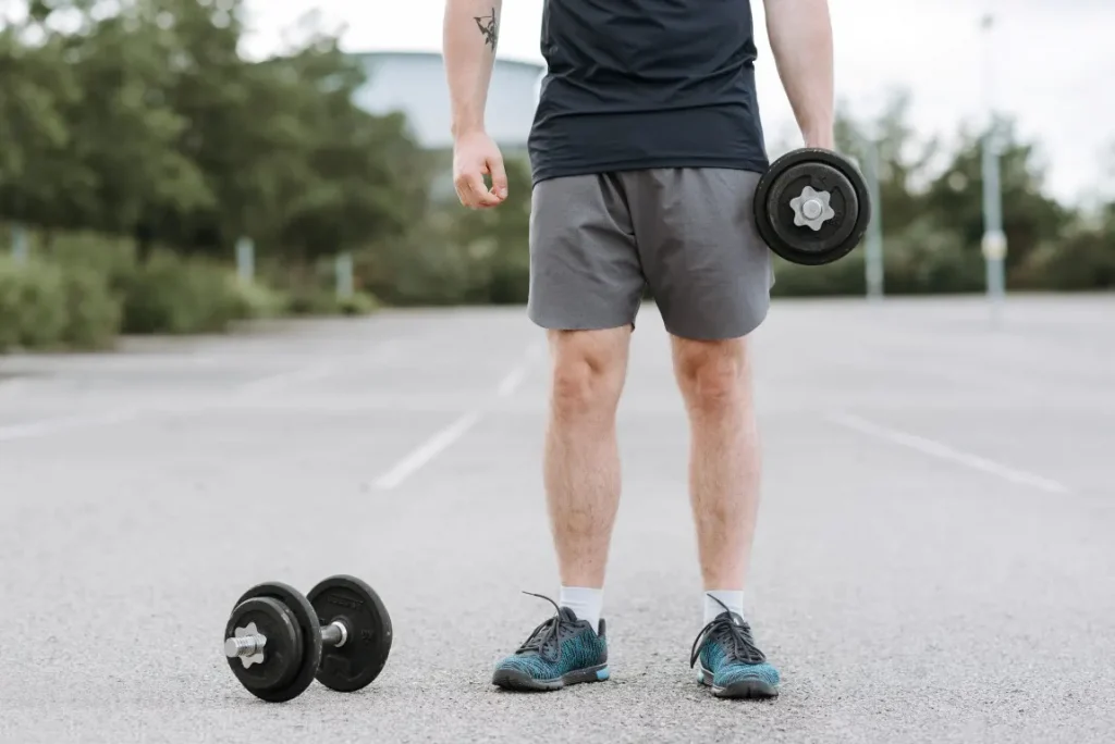 Strong man training with dumbbells on the sports ground