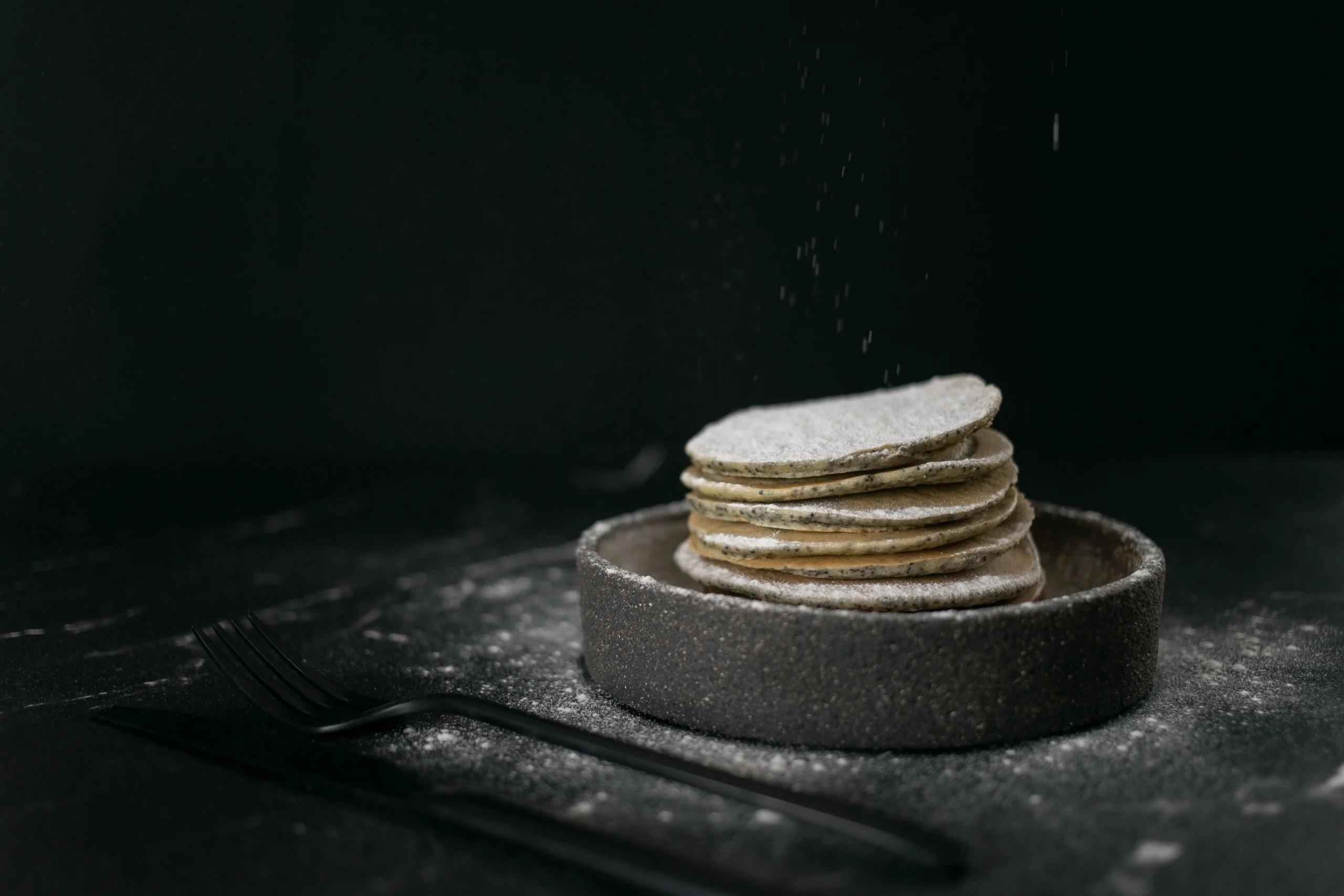 Tasty pancakes sprinkled with sugar powder on a dark matt dish