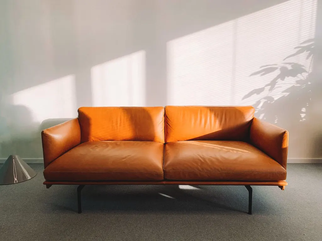 Two-seat orange leather sofa beside the wall in natural lighting