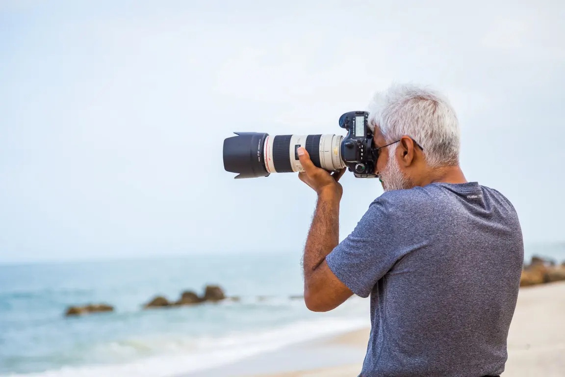 A man taking a photo with a telephoto lens from a beach