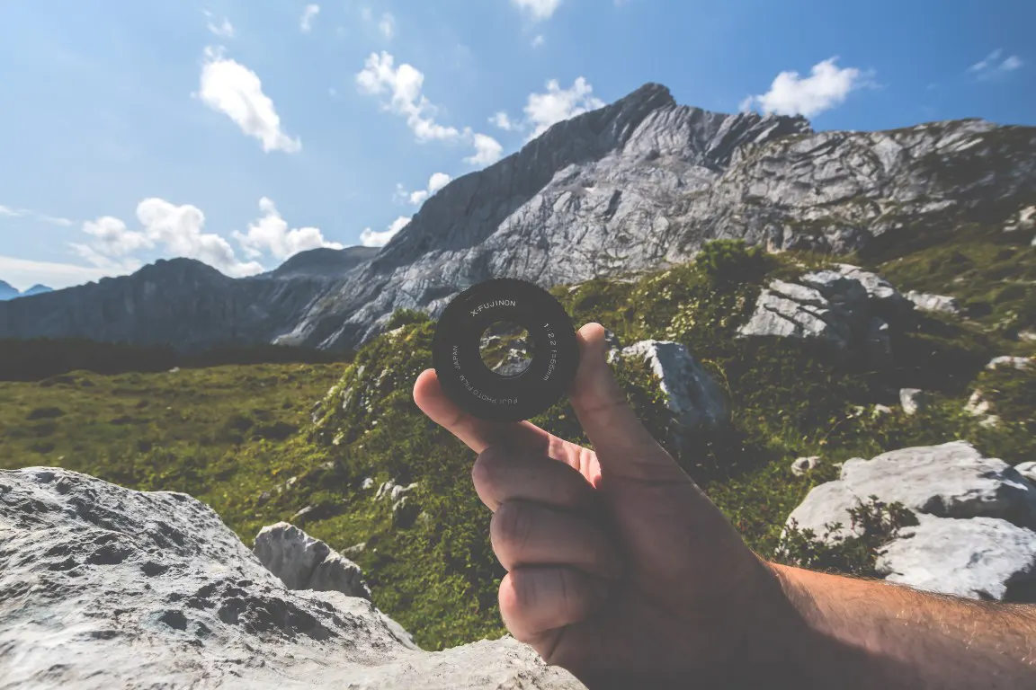 A photo of holding a camera lens near mountain on a hiking trail